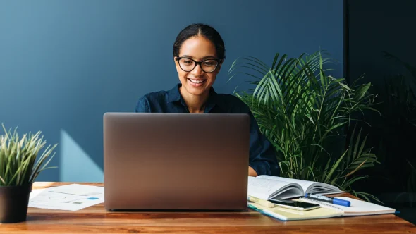 Smiling business woman sitting at a desk behind a laptop - Powered by Payroc - Sentry Bank