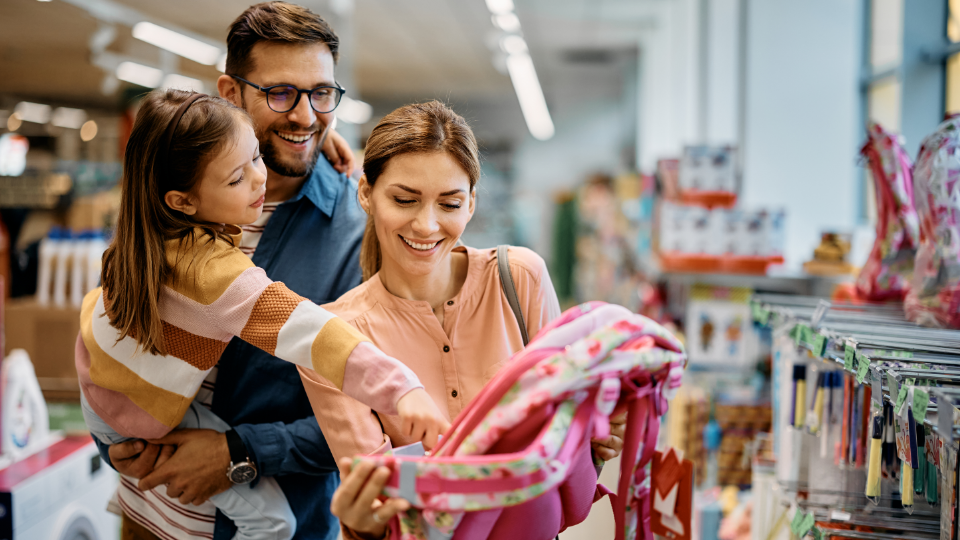 Happy family picking out a new backpack for the little girl in dad's arms