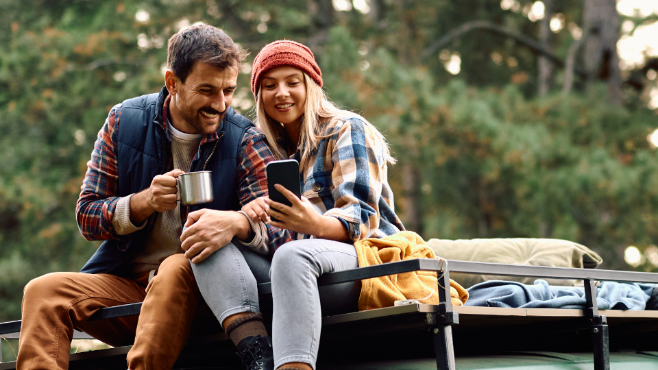 Couple sitting on top of a camper van looking at their Sentry Bank mobile app