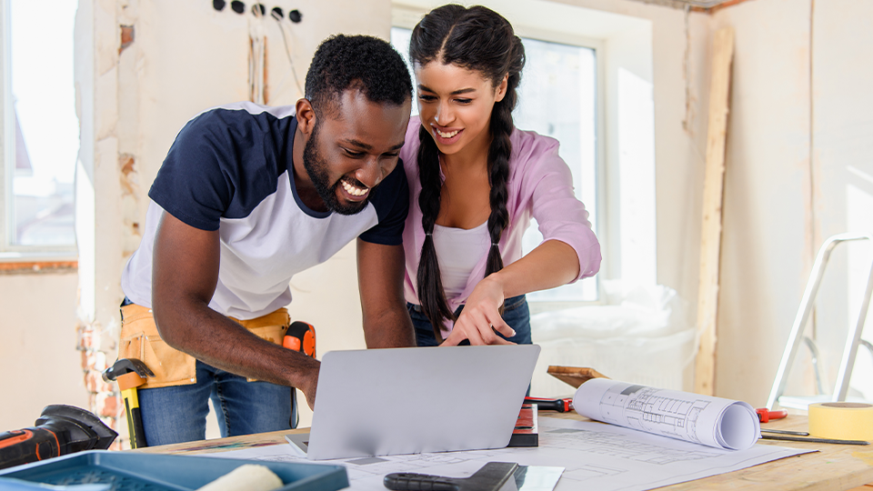 Couple looking at laptop inside a room of their house undergoing a remodel